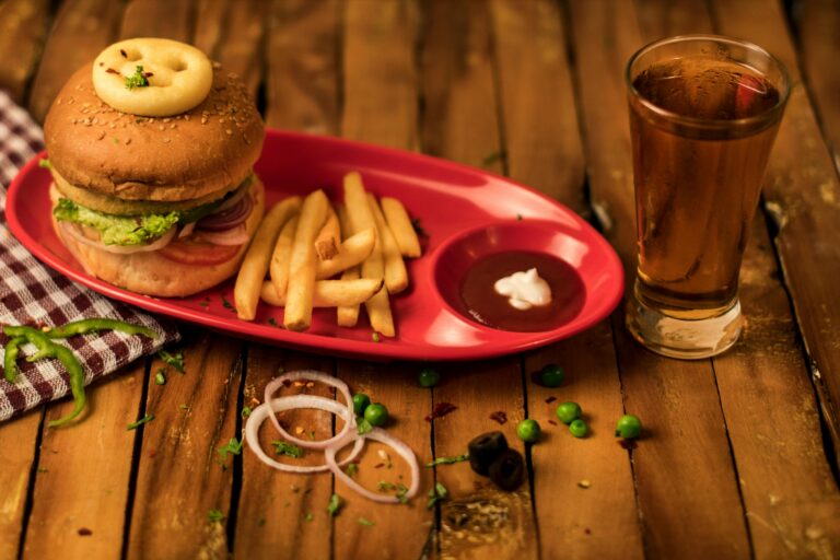 Close-up of a delicious burger with fries and drink on a rustic wooden table.